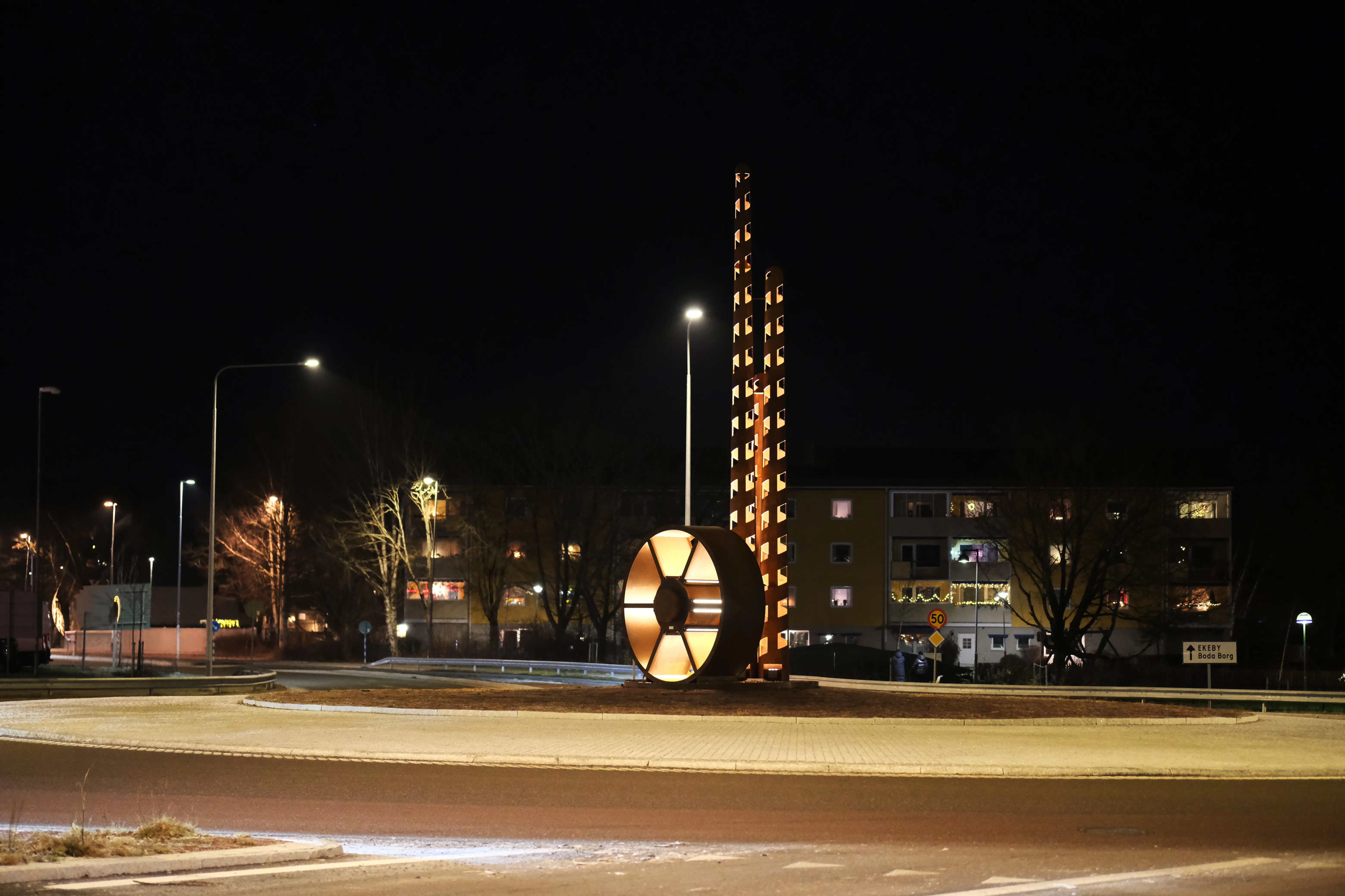 Konstverk i två delar i en rondell. Ena delen är konor i varierande höjder och andra delen är ett vattenhjul. 