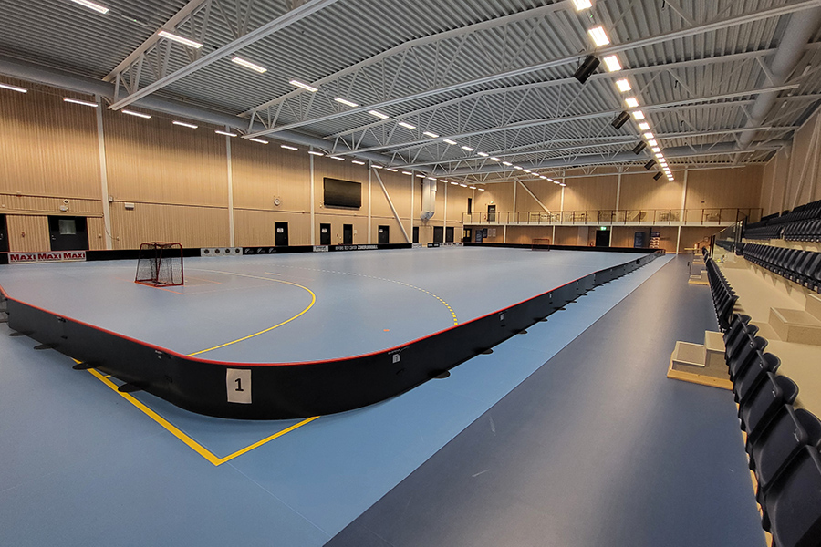 Idrottssal med blå golvbeläggning. Sarg för innebandy med innebandymål. Stolar och bord vid kortvägg. Publikplatser längs ena väggen, andra väggen har dörrar.