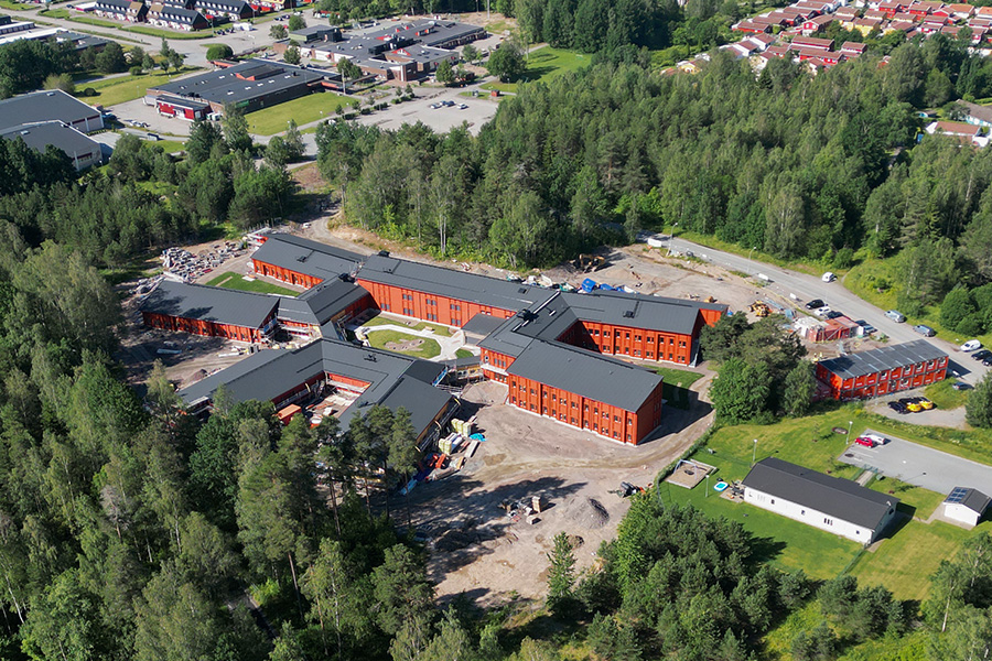Flygbild över en byggarbetsplats med en byggnad i mitten av bilden. Runtomkring står arbetsmaterial.