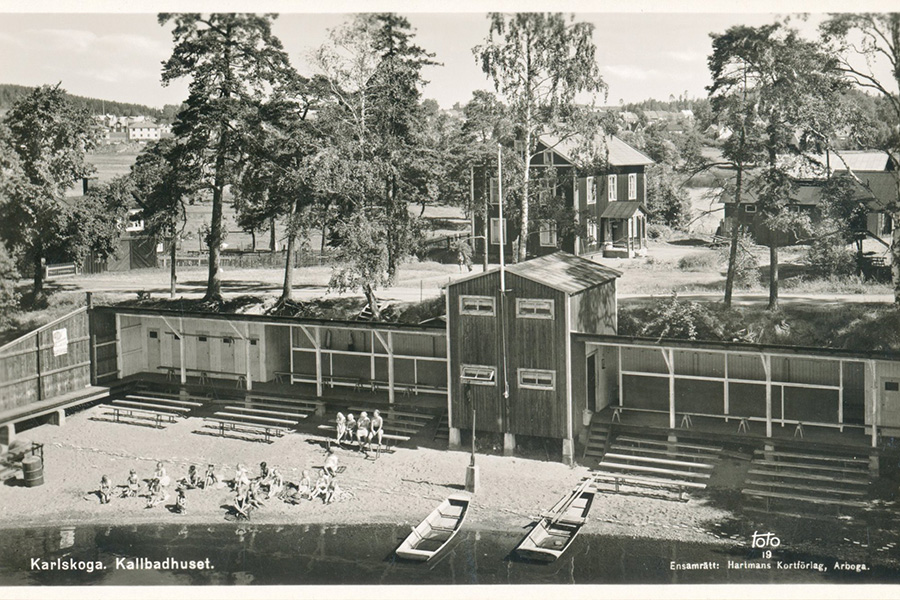 En svartvit bild som visar en byggnad på stranden där människor ligger och solar.