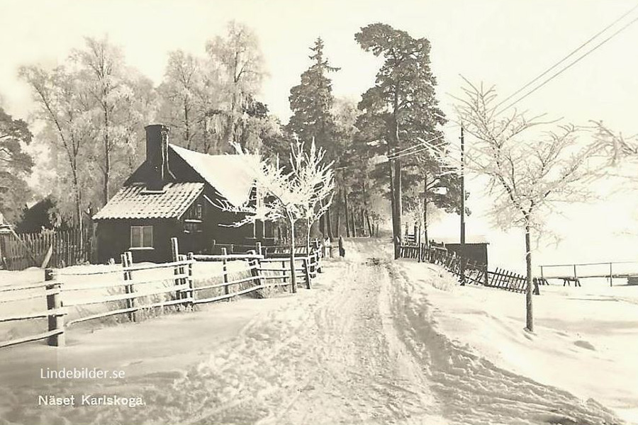 Ett snöigt landskap, vid sidan av ett stig ligger ett hus med ett staket framför. 