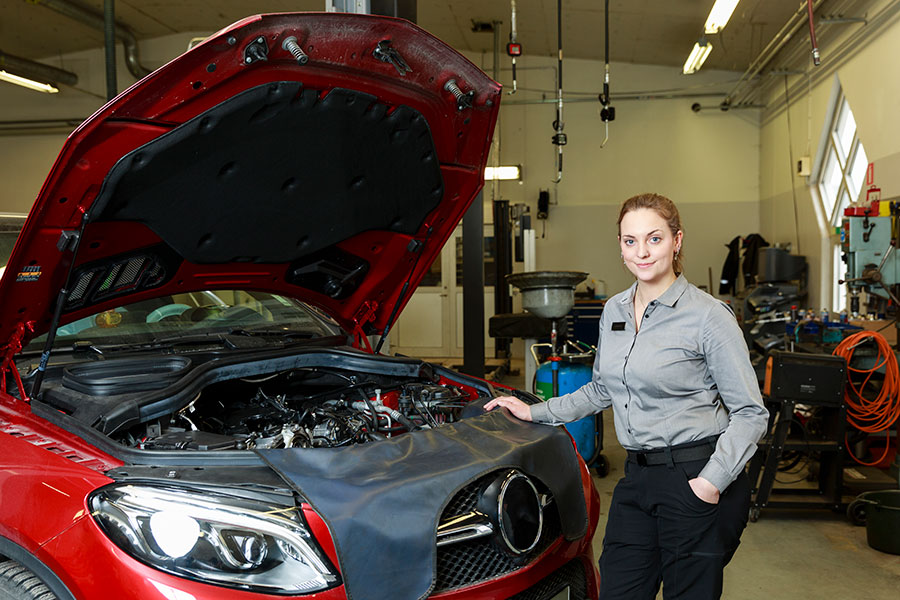 Bil med motorhuv öppen där kvinna står bredvid i arbetskläder.