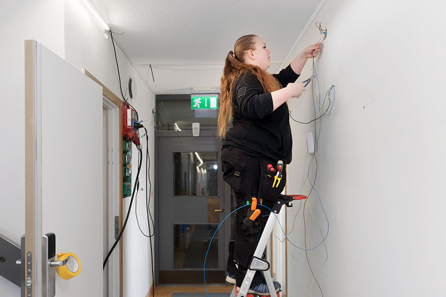 Kvinna som står vid stege och justerar elkablar i en fastighet.