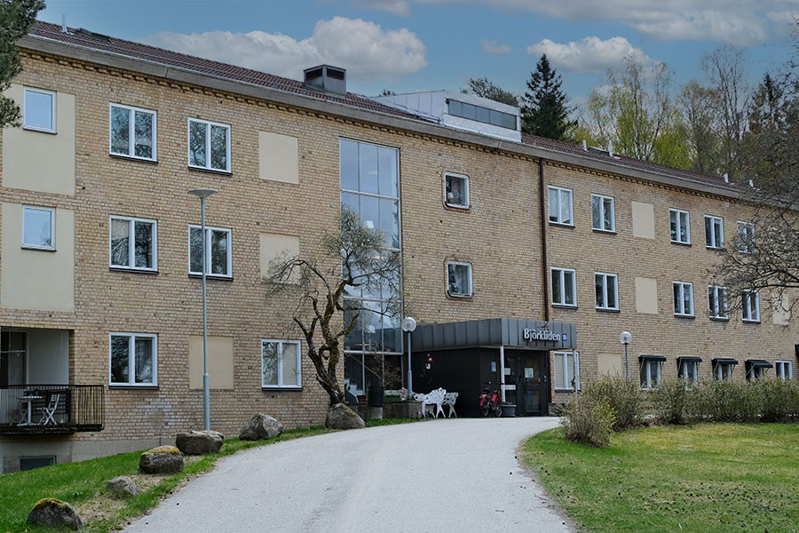 En tegelbyggnad med stora fönster. En grusgång leder fram till ingången.