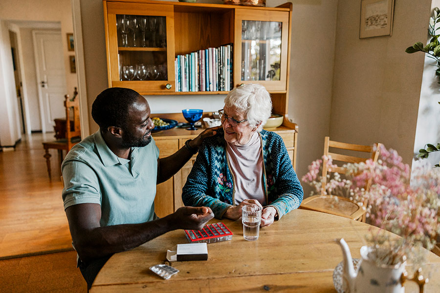 En yngre kille som hjälper en äldre dam att ta medicin.