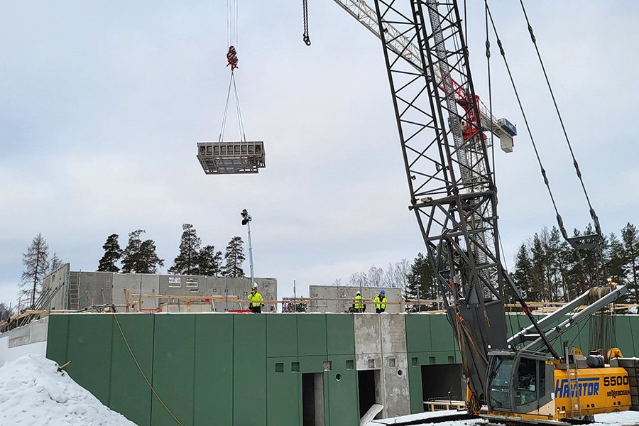 En byggarbetsplats där en kran lyfter en stor kvadratiskt metallpool.