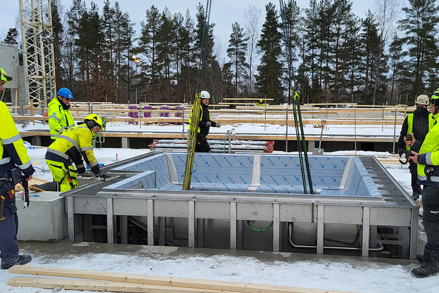 En byggarbetsplats där flera personer i varselkläder arbetar runt en metallpool. 
