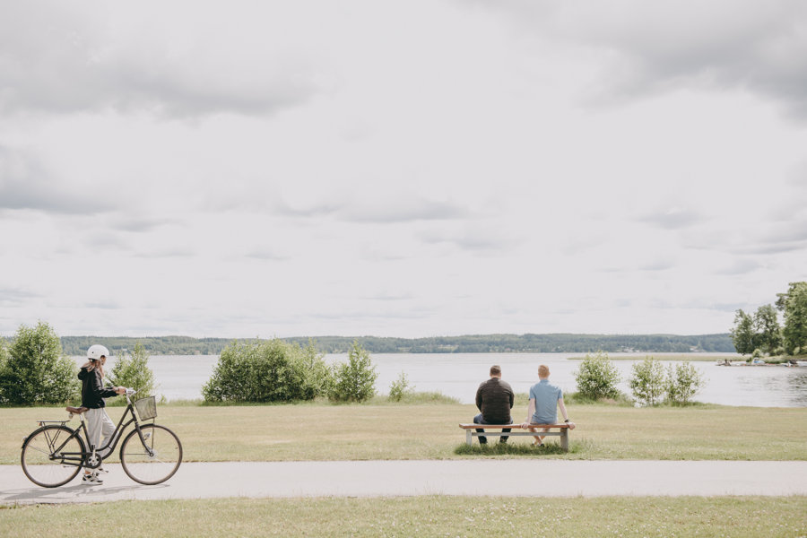 Cyklist vid sjö där två sitter på parkbänk.