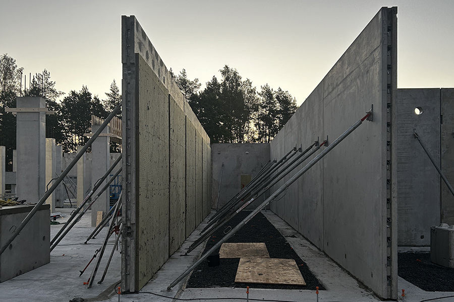 En byggarbetsplats med betongväggar. Mot betongväggarna står pinnar i metall lutade. 