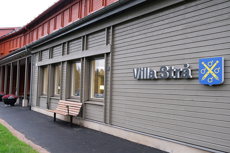 EN fasad med röd och grå träpanel. TIll höger står en skylt med texten "Villa strå"