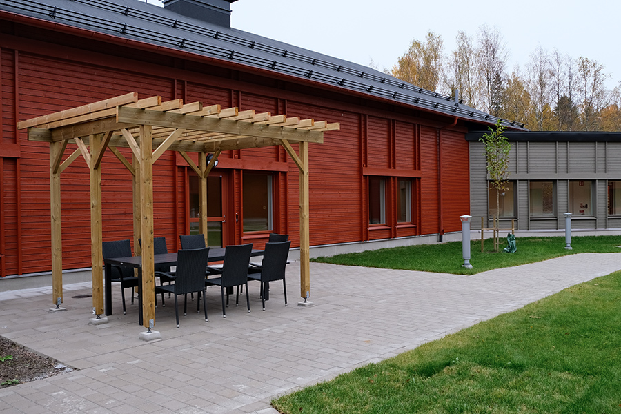 En innergård med gräsmatta och stenplattor. Till vänster står en pergola.