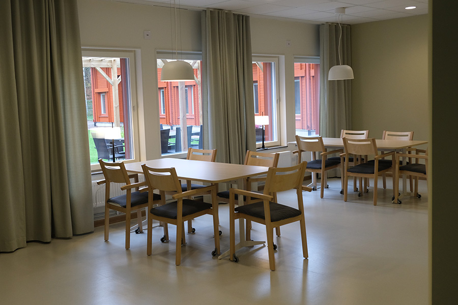 Ett rum med ljusa väggar och fönster. Vid fönstren står två bord med stolar runt omkring.