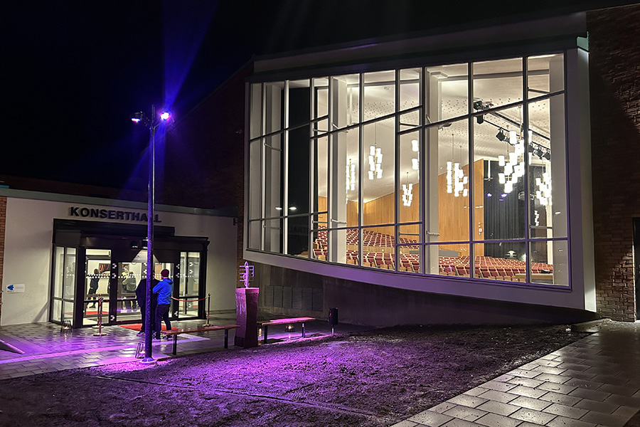 En byggnad upplyst med färgade lampor. På fasaden står det Konserthall.