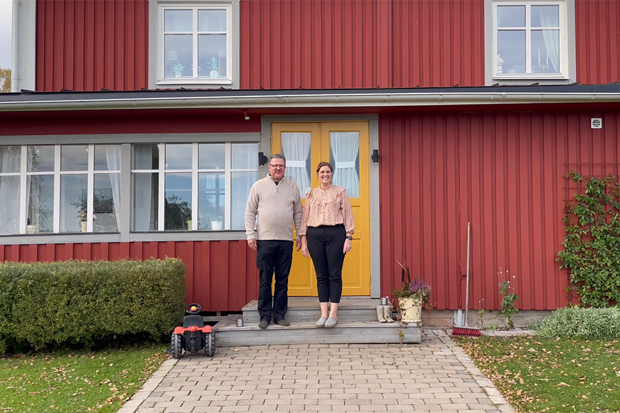 En man och en kvinna står på trappan utanför sitt hus. De ser båda glada ut.