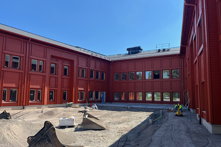 Flygbild över en byggarbetsplats med en byggnad i mitten av bilden. Runtomkring står arbetsmaterial.