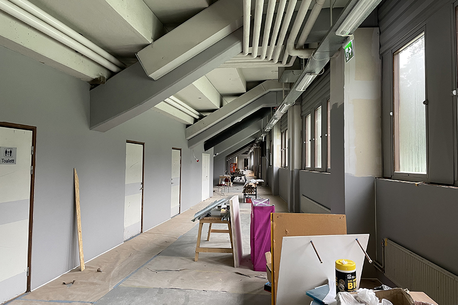 En korridor som renoveras. Byggmaterial så som träskivor och färgburkar står längs väggen. 