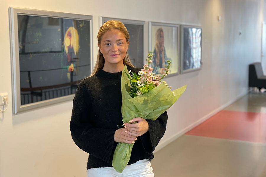 Tjej står och kollar in i kameran med en blombukett i handen