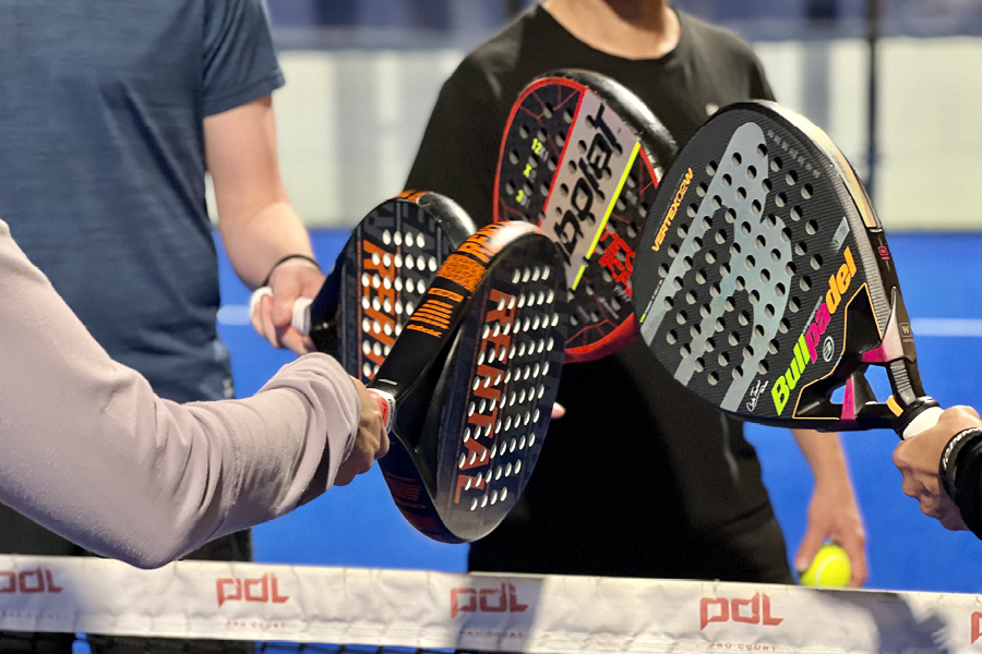 Ett tennisrack i närbild. Framför ligger en tennnisboll. 