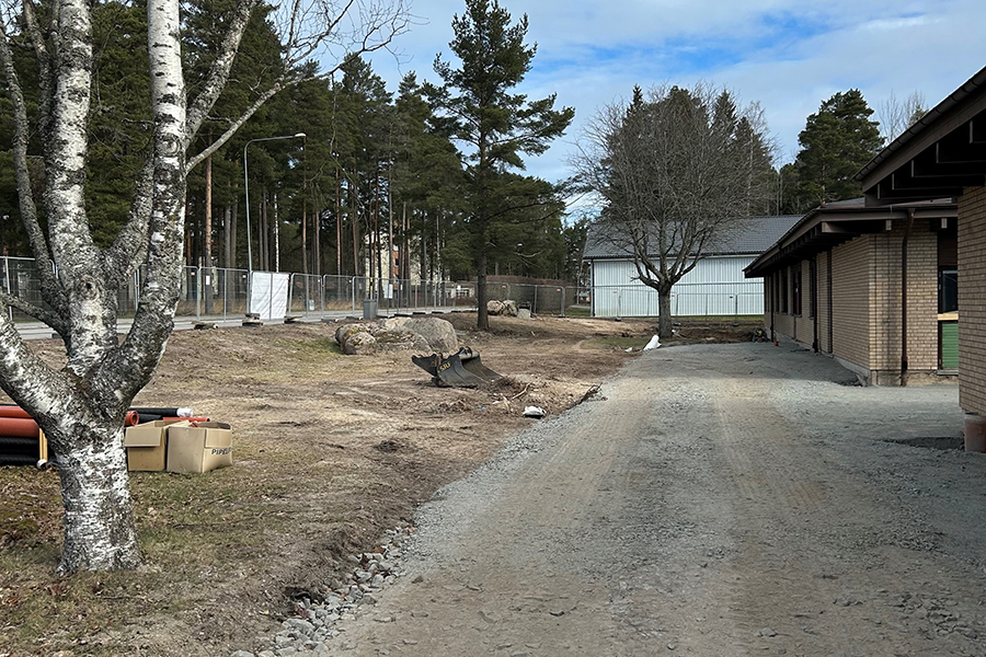 En utegård utanför en gul tegelbyggnad. Marken är till hälften täckt av lera och hälften är uppgrusad.