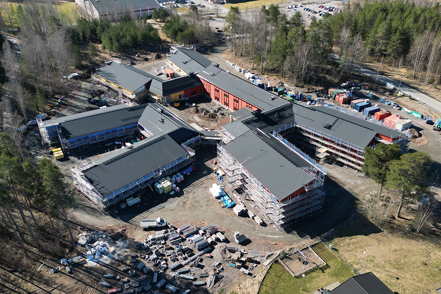 Flygbild över en byggarbetsplats med en byggnad i mitten av bilden. Runtomkring står arbetsmaterial.