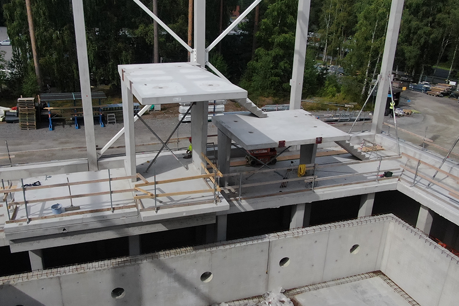 Byggarbetsplats med betongkonstruktion och stålpelare. En person i reflexväst syns på avstånd.