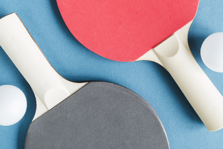 Ett svart och ett rött bordtennisrack. Vid sidan om racketen ligger två bordtennisbollar.