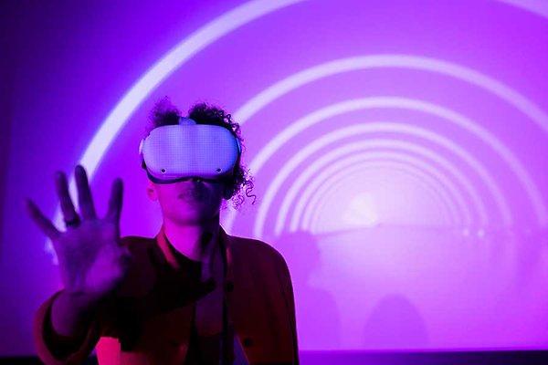 En person bär en VR-headset och sträcker ut handen mot en bakgrund av lila och vita ljusstrimmor.