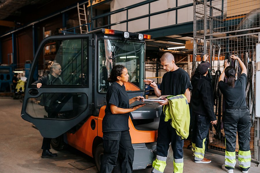 Flera personer i arbetskläder står i lager och arbetar.