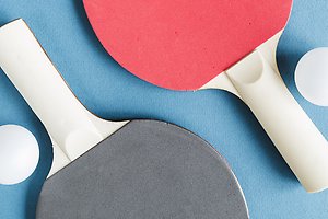 Ett svart och ett rött bordtennisrack. Vid sidan om racketen ligger två bordtennisbollar.