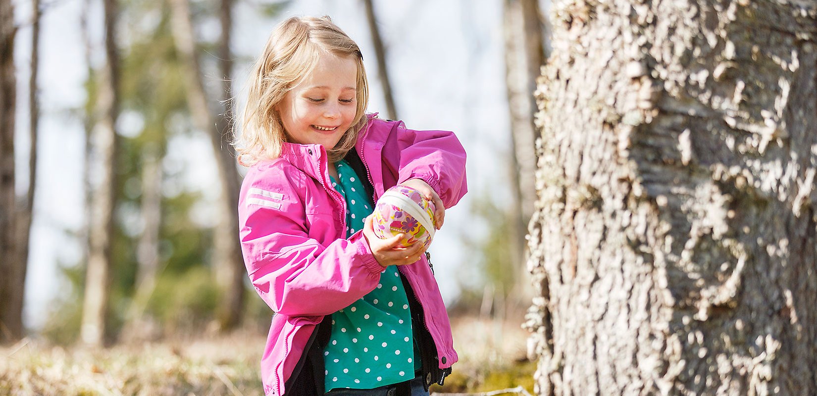 En flicka som letar påskägg ute i naturen.