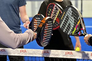 Ett tennisrack i närbild. Framför ligger en tennnisboll. 