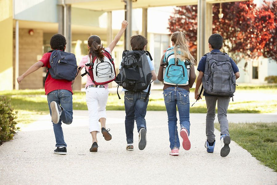 Fem elever springer mot entrédörren på skolan med ryggsäckar på ryggen. 